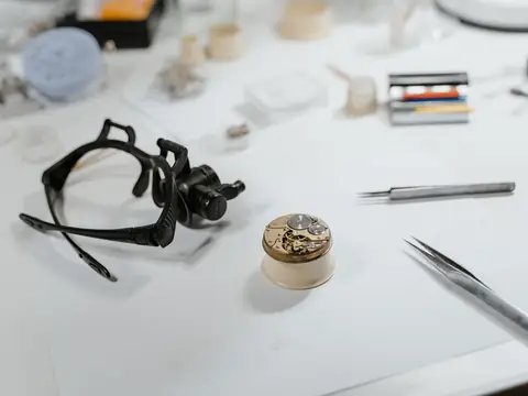 A watchmaker's loupe, two pairs of tweezers and a watch movement on a holder laid out on a workbench